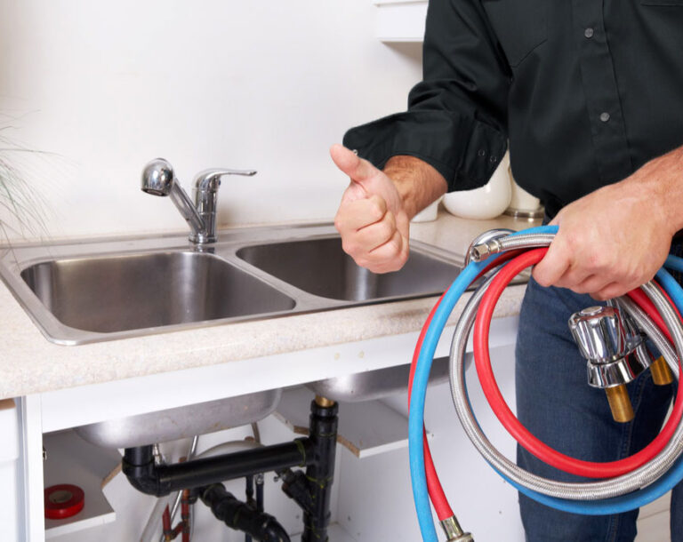 Plombier tenant des flexibles d’alimentation en eau devant un évier double.